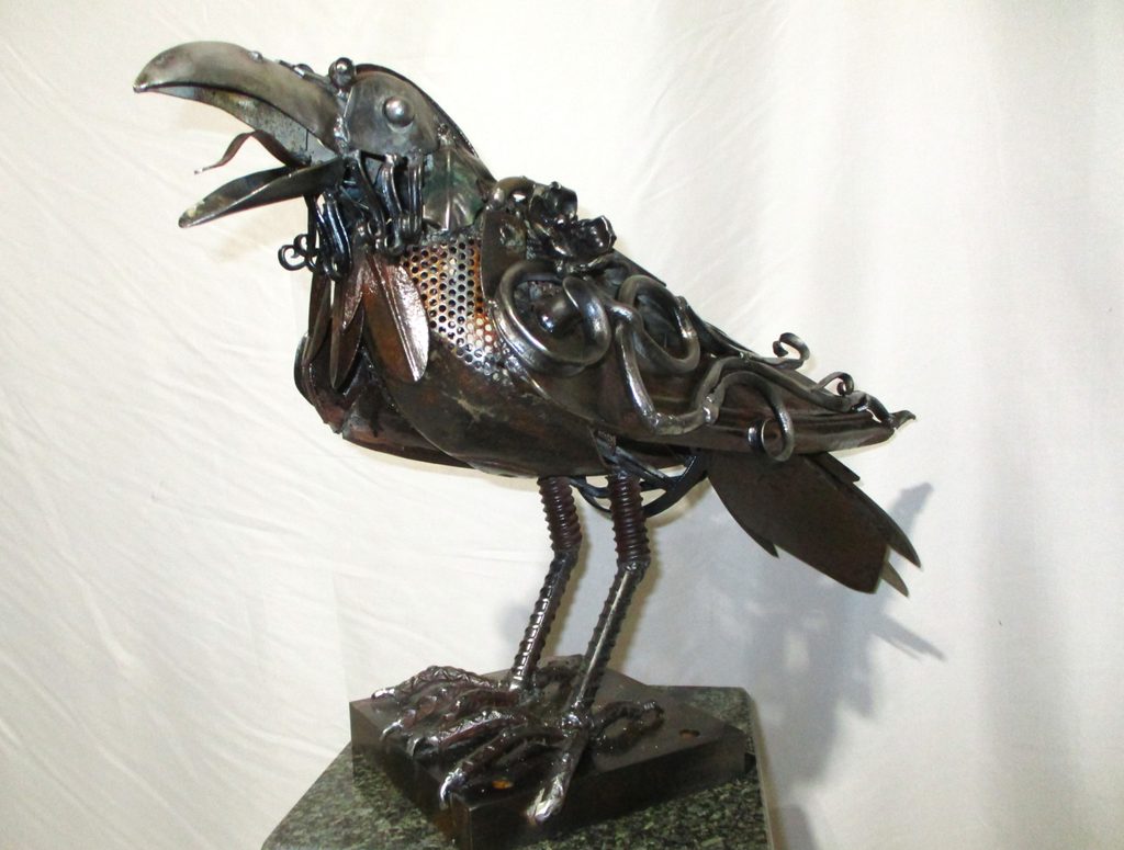 Mixed media sculpture of a raven, an assemblage of various metal components, perched with its beak open. 