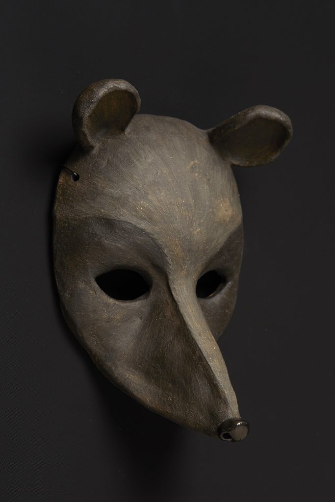 Wooden mask with wide eye holes, and long rodentlike-snout, and small round ears. 